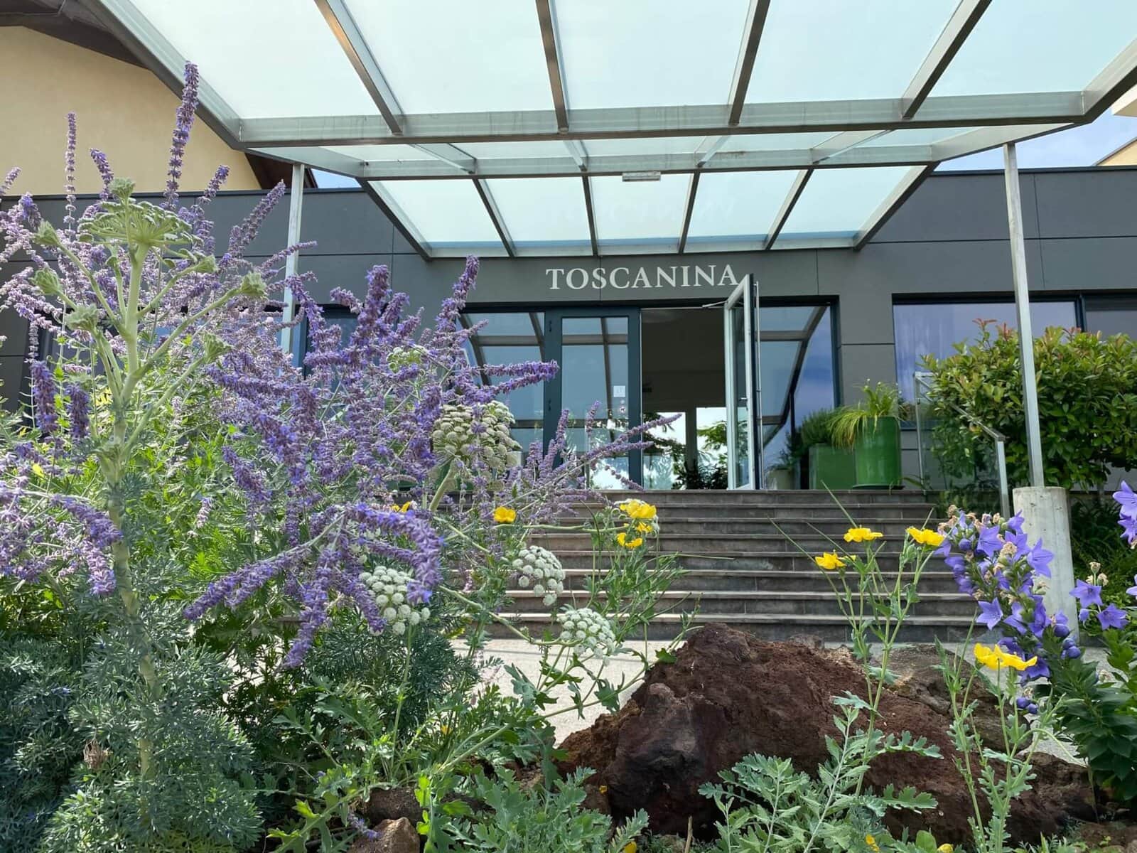 Modernes Hotel Toscanina mit blühendem Garten und einladender Eingangstreppe.