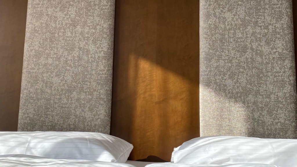 Gemütliches Hotelzimmer mit Betten und modernem, geradlinigem und gepolsterten Betthaupt, ideal für Ihren Sommer-Urlaub.