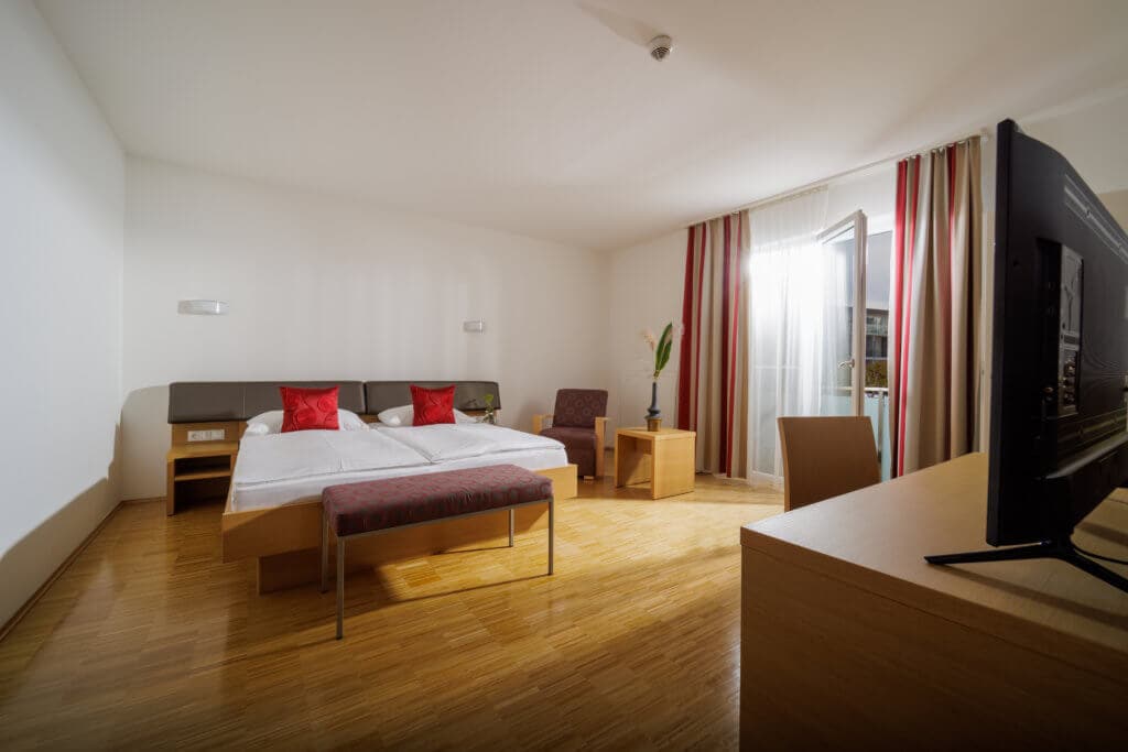 Modernes Hotelzimmer im Toscanina mit Doppelbett, TV und Balkon.