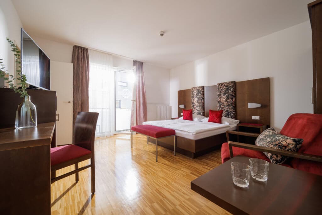 Modernes Hotelzimmer im Toscanina mit Doppelbett, Sitzbereich und Balkonzugang.