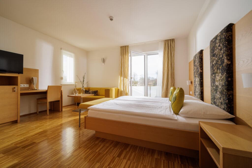 Modernes und helles Hotelzimmer im Toscanina mit Balkon, Holzfußboden und gemütlicher Einrichtung.