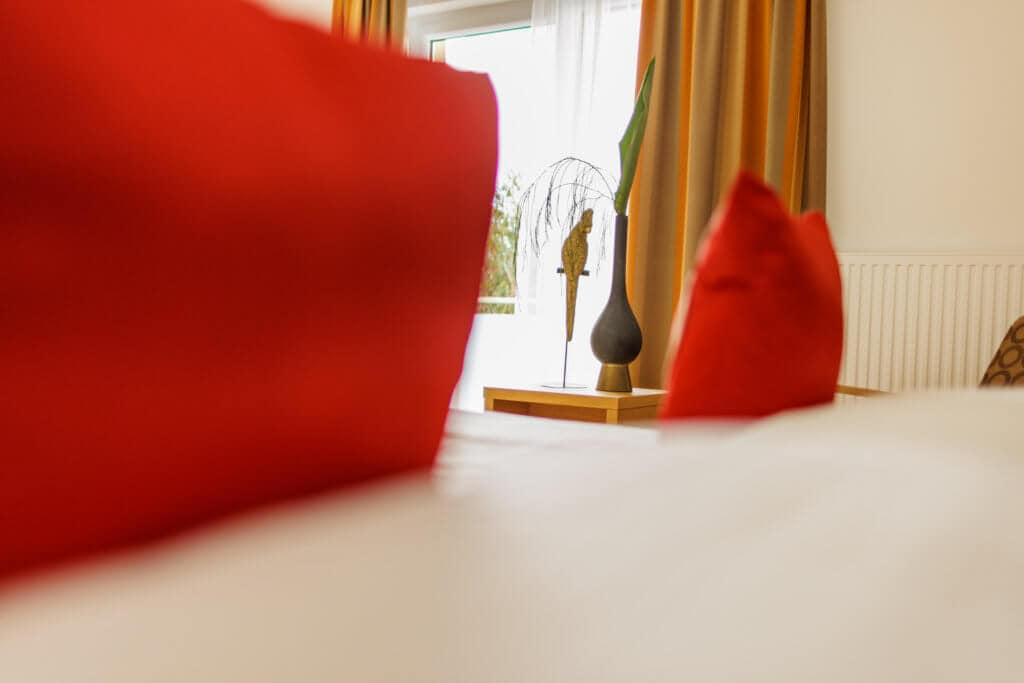 Gemütliches Hotelzimmer im Toscanina mit roten Kissen und natürlichem Licht.