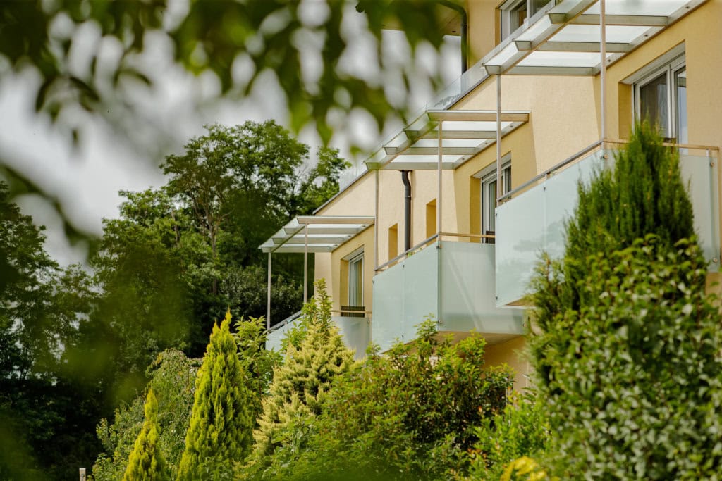Balkon mit Blick auf grüne Gartenlandschaft und Hotelgebäude.
